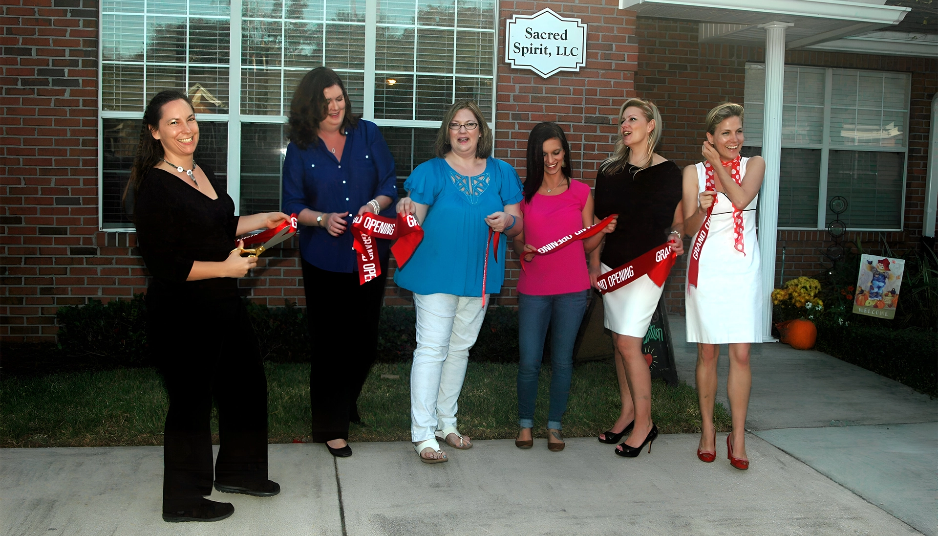 A group of people standing outside holding red ribbon.