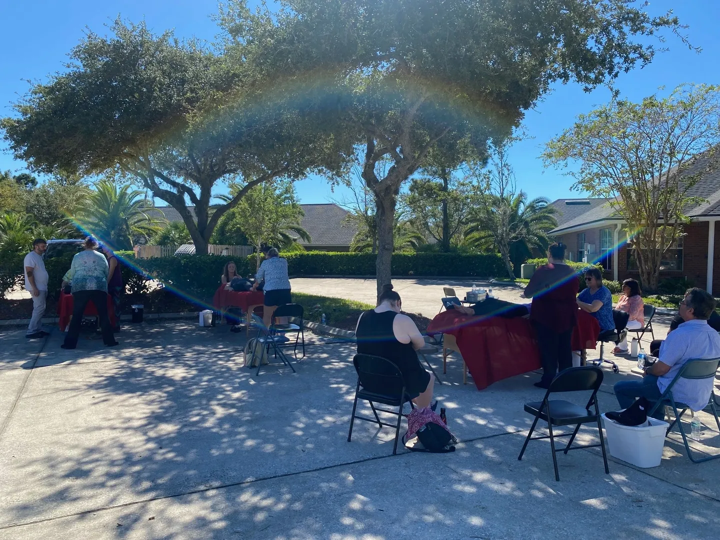 A group of people sitting under trees on the sand.